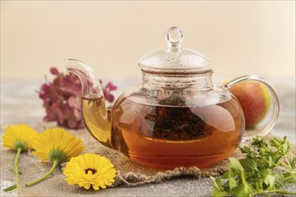 Red tea with herbs in glass teapot on brown concrete background and linen textile. Healthy drink