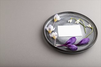 White paper invitation card, mockup with crocus and galanthus flowers on ceramic plate and gray