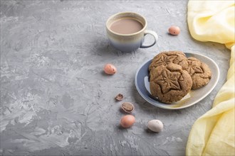 Homemade oatmeal cookies with a cup of cocoa and a yellow textile on a gray concrete background.