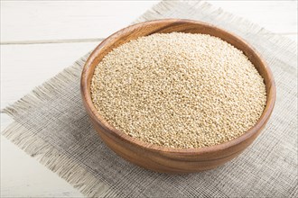 Wooden bowl with raw white quinoa seeds on a white wooden background and linen textile. Side view,