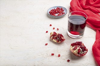 Glass of pomegranate juice on a white concrete background with red textile. Side view, copy space,