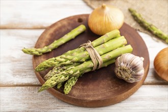 Bunch of fresh green asparagus, garlic, onion on white wooden background. Side view, selective