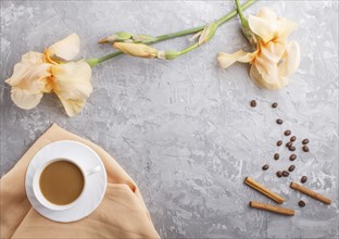 Orange iris flowers and a cup of coffee on a gray concrete background. Morninig, spring, fashion