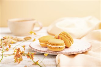 Orange macarons or macaroons cakes with cup of apricot juice on a white wooden background and