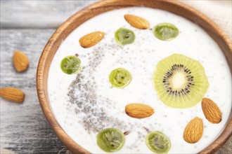 Yogurt with kiwi, gooseberry, chia and almonds in wooden bowl on gray wooden background and linen