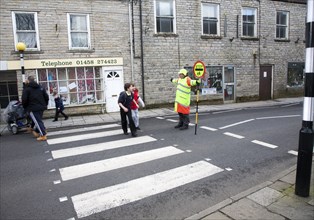 Lollipop man stopping traffic to allow people to cross the road safely, Somerton, Somerset,