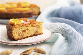 Orange cake with almonds and a cup of coffee on a white concrete background and blue linen textile.