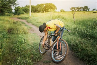 Man repairing his bike in the middle of the road. Man in the countryside repairing his bike