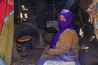 Nomadic Bedouin woman with hijab baking bread in traditional oven in tent in the Sahara Desert near