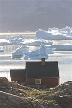 Typical Greenlandic house in front of icebergs by the sea, summer, sunny, Uummannaq, West