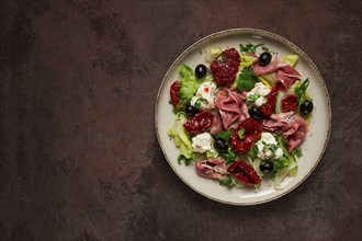 Salad with dried tomatoes, prosciutto, soft cheese, olives, homemade, top view