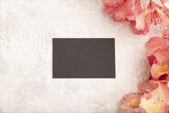 Black business card with pink azalea flowers on gray concrete background. top view, flat lay, copy