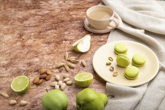 Green macarons or macaroons cakes with cup of coffee on a brown concrete background and linen