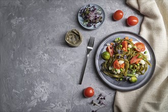 Tagliatelle green spinach pasta with tomato, pea and microgreen sprouts on a gray concrete