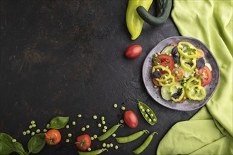 Vegetarian salad from green pea, tomatoes, pepper and basil on a black concrete background and