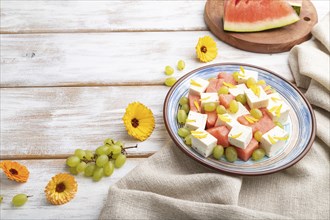 Vegetarian salad with watermelon, feta cheese, and grapes on blue ceramic plate on white wooden