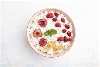 Rice flakes porridge with milk and strawberry in ceramic bowl on white concrete background. Top