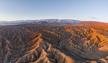 Riverbed in a landscape of eroded hills, badlands at sunrise, Issyk Kul Lake in the background,