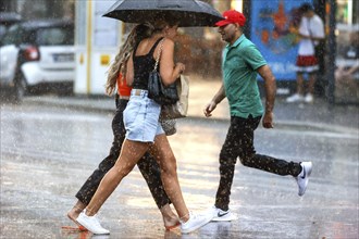 Two woman and a man run across Potsdamer Strasse in heavy rain. After weeks of heat, the first