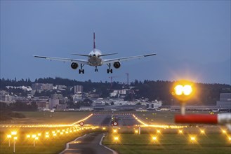 Aircraft of the airline Swiss landing in the evening with illuminated runway. Zurich Airport,