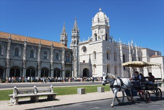 Eine gotische Kathedrale unter klarem blauen Himmel mit Touristen und einer Kutsche mit Pferden im