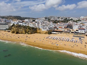 Coastal town with sandy beach, many bathers and buildings along the coast, aerial view, Albufeira,