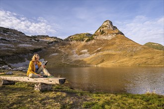 Lake Augstsee and the Atterkogel mountain on the Loser. A hiker sits on a bench and reads a book.