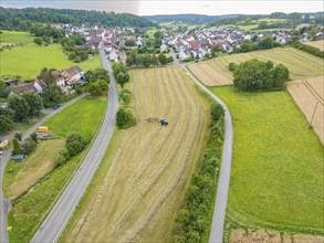 Aerial view of a village, surrounded by fields and roads, with a tractor on a hay field, Dachtel.