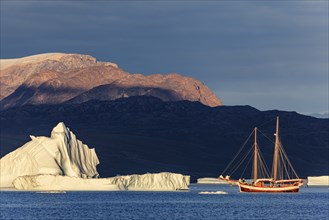 Sailing boat, ship in fjord in front of large icebergs and mountains, evening light, Scoresby