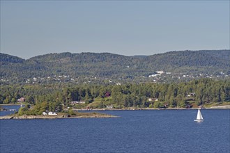 A lonely sailing boat near a small island, surrounded by water and with wooded hills in the