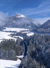 An idyllic snowy landscape with a road winding through the forest under a clear blue sky,