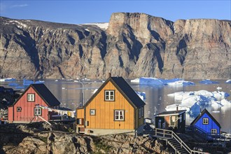 Typical Greenlandic houses in front of icebergs, Inuit settlement, summer, sunny, Uummannaq, West