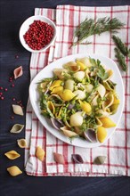 Conchiglie colored pasta with fresh greengrocery on a linen tablecloth on black wooden background.