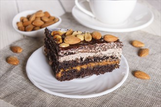 Chocolate cake with caramel, peanuts and almonds on a white wooden background. cup of coffee, close