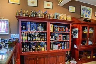 Inviting interior view of a bar with a selection of alcohol bottles on red wooden shelves and