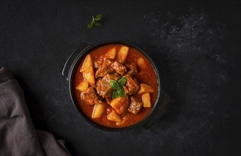 Stew with potatoes, in tomato sauce, with spices and herbs, close-up, no people, on a black