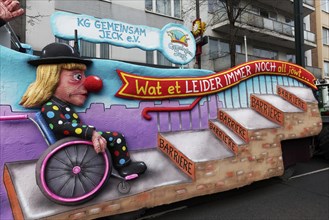 Wheelchair user in jester's costume waiting in front of steps, papier-mâché figure, motif float on