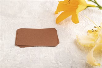 Brown paper business card mockup with orange day-lily flower on gray concrete background. Blank,