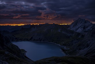 Lake Lüner See with Montafon mountains and dramatic cloudy sky at sunrise, Tschagguns, Rätikon,