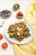 Tagliatelle green spinach pasta with tomato, pea and microgreen sprouts on a white wooden