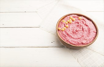 Hummus with beet in wooden bowl on a white wooden background and linen textile. Side view, copy