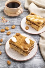 Honey cake with milk cream, caramel, almonds and a cup of coffee on a gray wooden background and