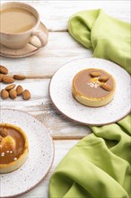 Sweet tartlets with almonds and caramel cream with cup of coffee on a white wooden background and