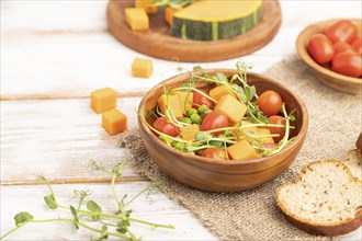 Vegetarian vegetable salad of tomatoes, pumpkin, microgreen pea sprouts on white wooden background