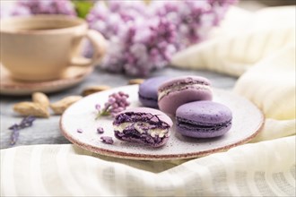 Purple macarons or macaroons cakes with cup of coffee on a gray wooden background and white linen