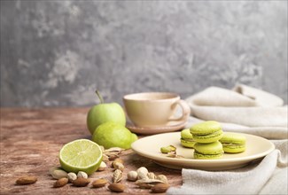 Green macarons or macaroons cakes with cup of coffee on a brown and gray concrete background and