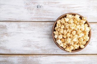 Popcorn with caramel in wooden bowl on a white wooden background. Top view, flat lay, copy space