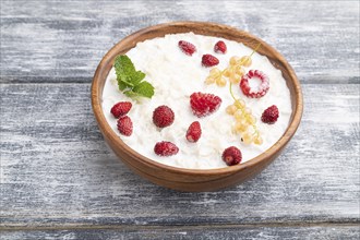 Rice flakes porridge with milk and strawberry in wooden bowl on gray wooden background. Side view,