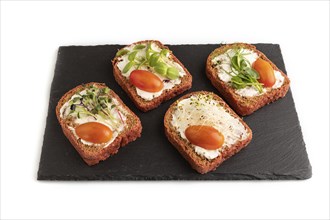 Red beet bread sandwiches with cream cheese, tomatoes and microgreen on black board isolated on