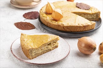 Autumn onion pie decorated with leaves and cup of coffee on gray concrete background. Side view,